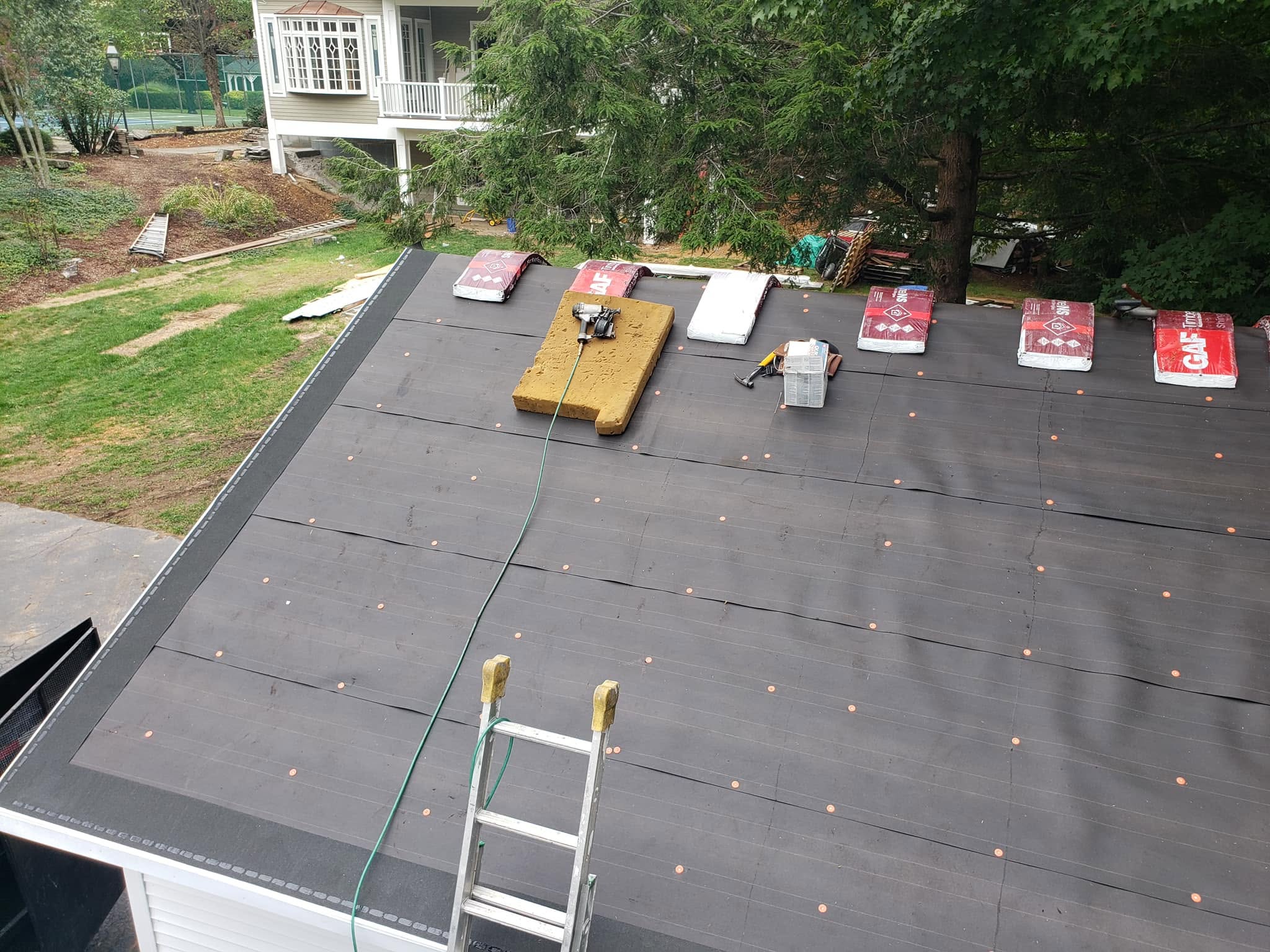 Residential roof installation in progress with dark shingles, fasteners, and materials laid out during construction