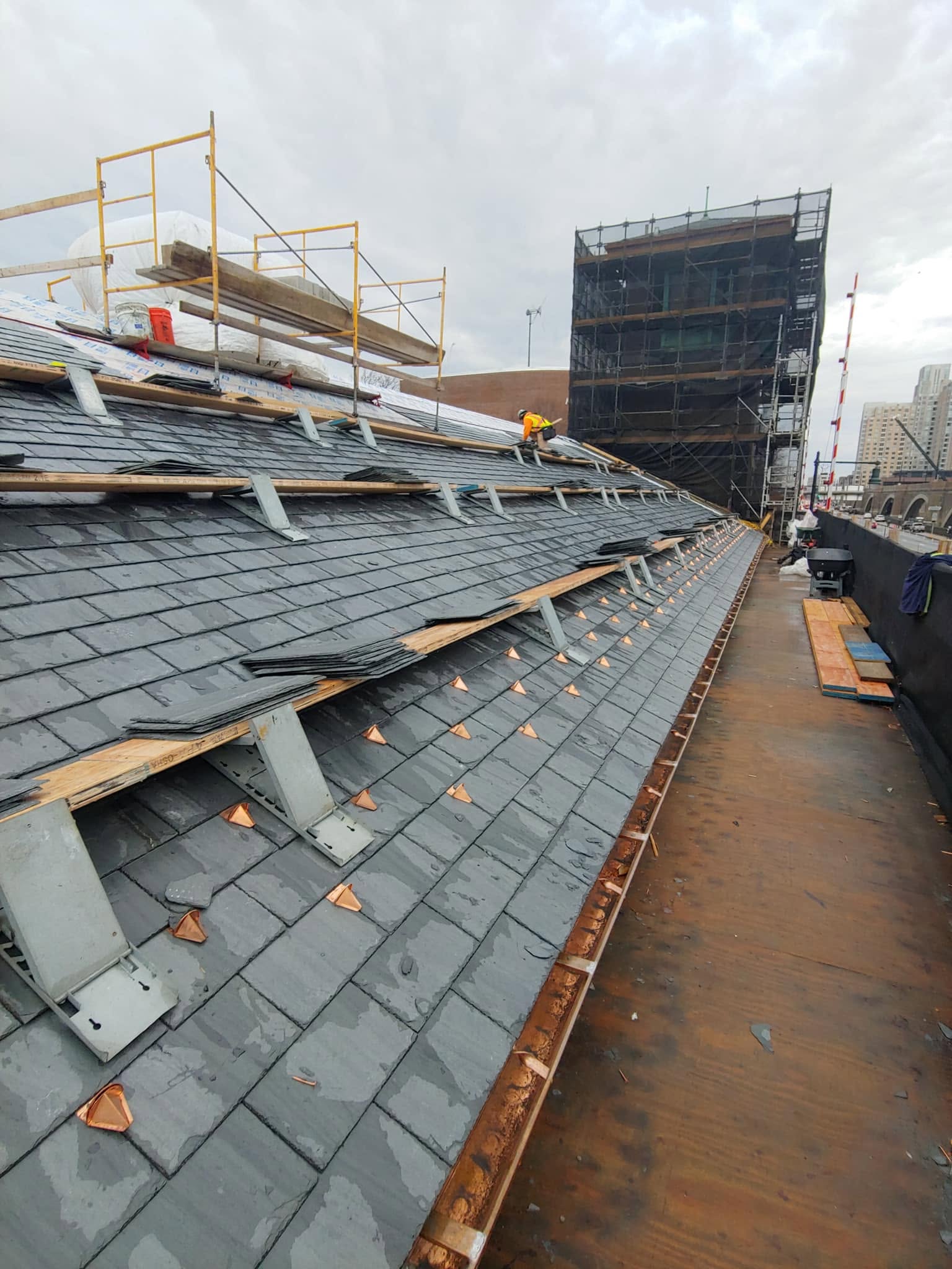 Roofing crew installing slate tiles on commercial building with safety scaffolding