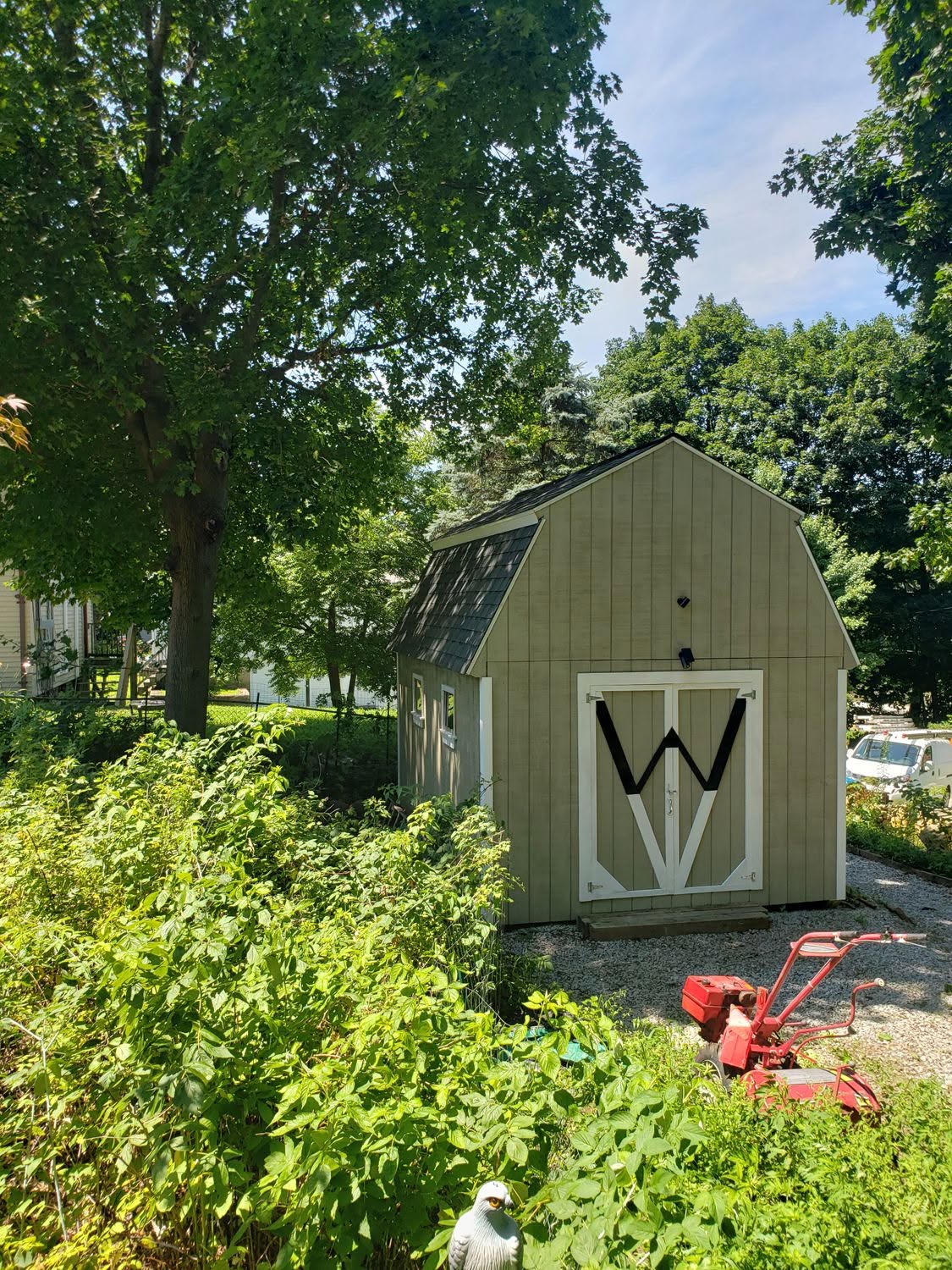 Sage green shed with white barn doors in landscaped yard surrounded by trees